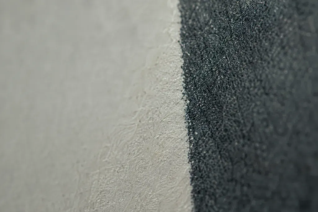 Extreme macro of the edge of a printed area on paper, where dense dark ink meets the unprinted margin and the paper fibre is visible.
